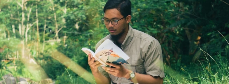 young guy reading a paperback in the forest